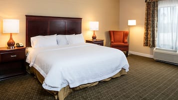 A hotel room with a large bed, two bedside tables with lamps, a chair, and a window with curtains.