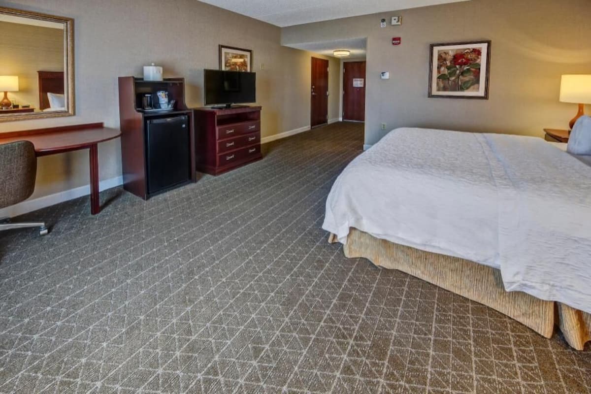 A hotel room with a bed, desk, TV, and dresser.