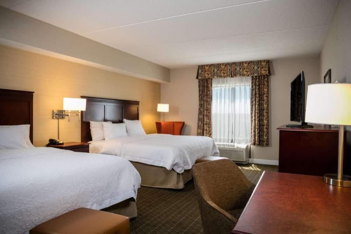 A hotel room with two beds, a desk, a TV, and a window with curtains.