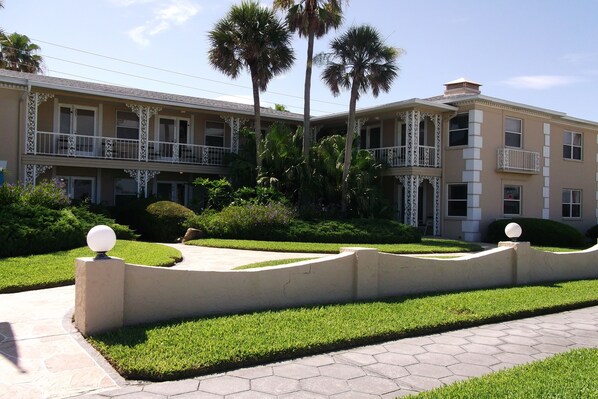A multi-story hotel with balconies, palm trees, and a well-maintained lawn.