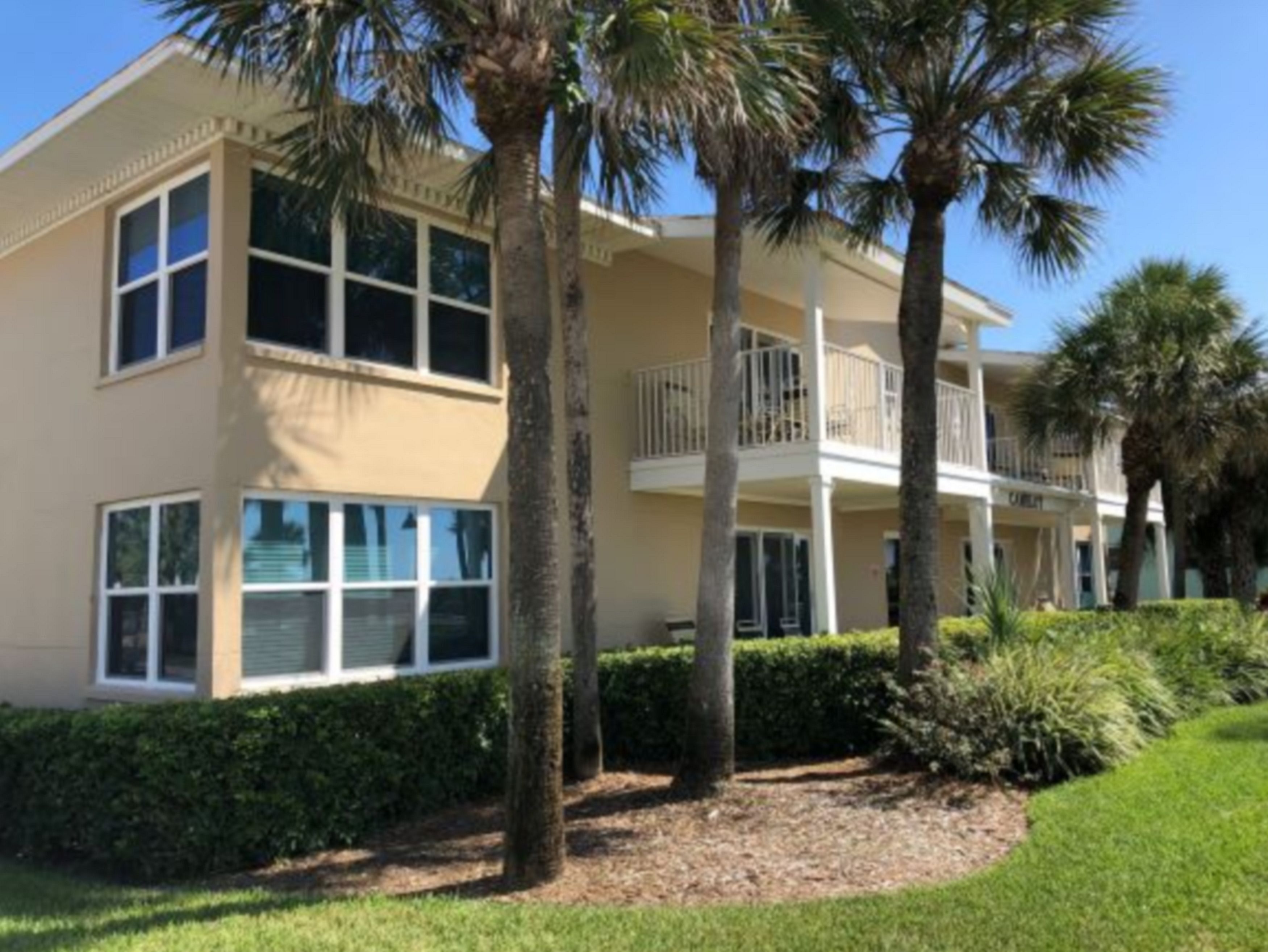 A multi-story hotel with balconies, palm trees, and a well-maintained lawn.