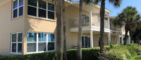 A multi-story hotel with balconies, palm trees, and a well-maintained lawn.
