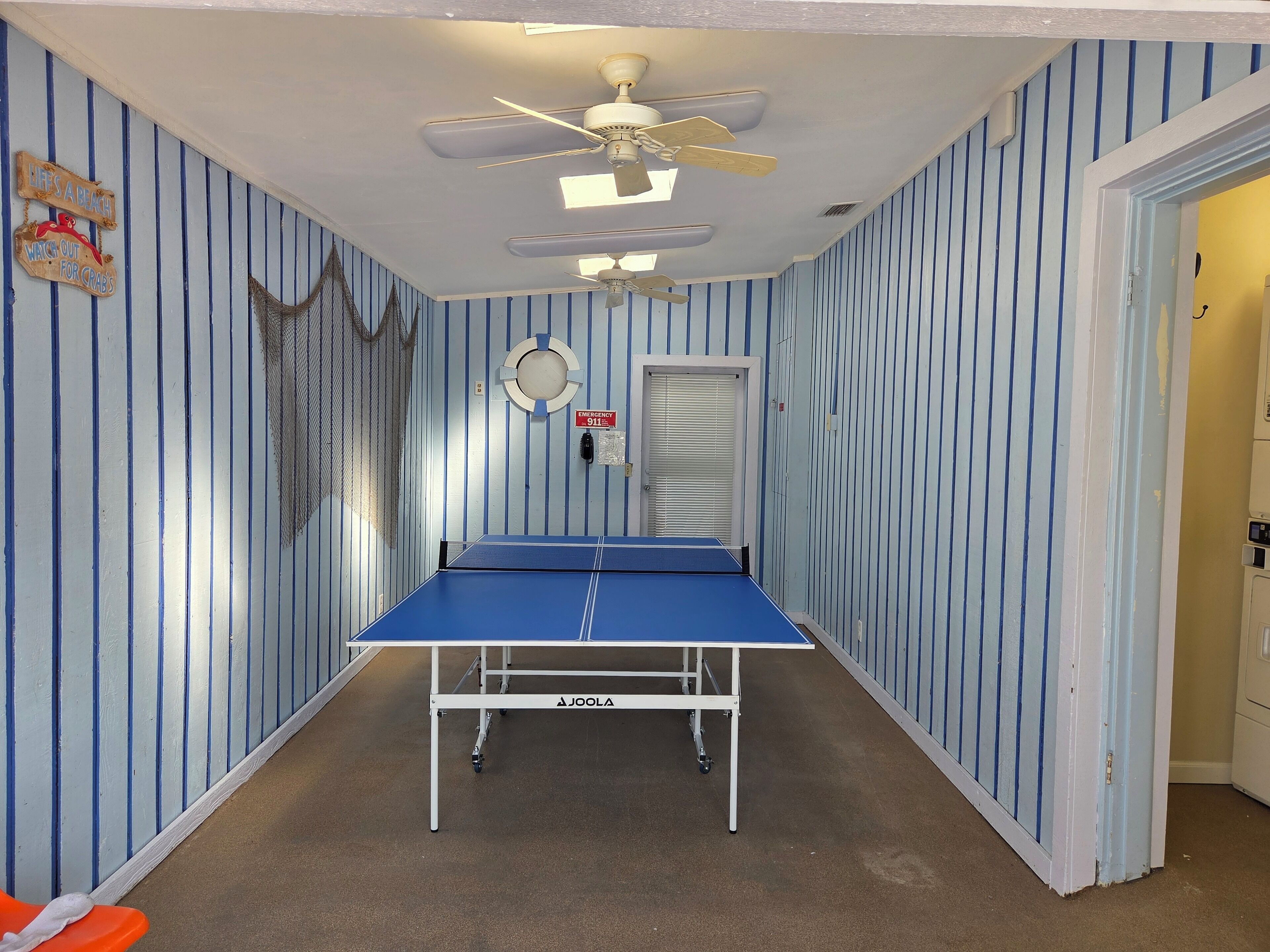 Et værelse med et pingpongbord, en loftventilator og stribede vægge.