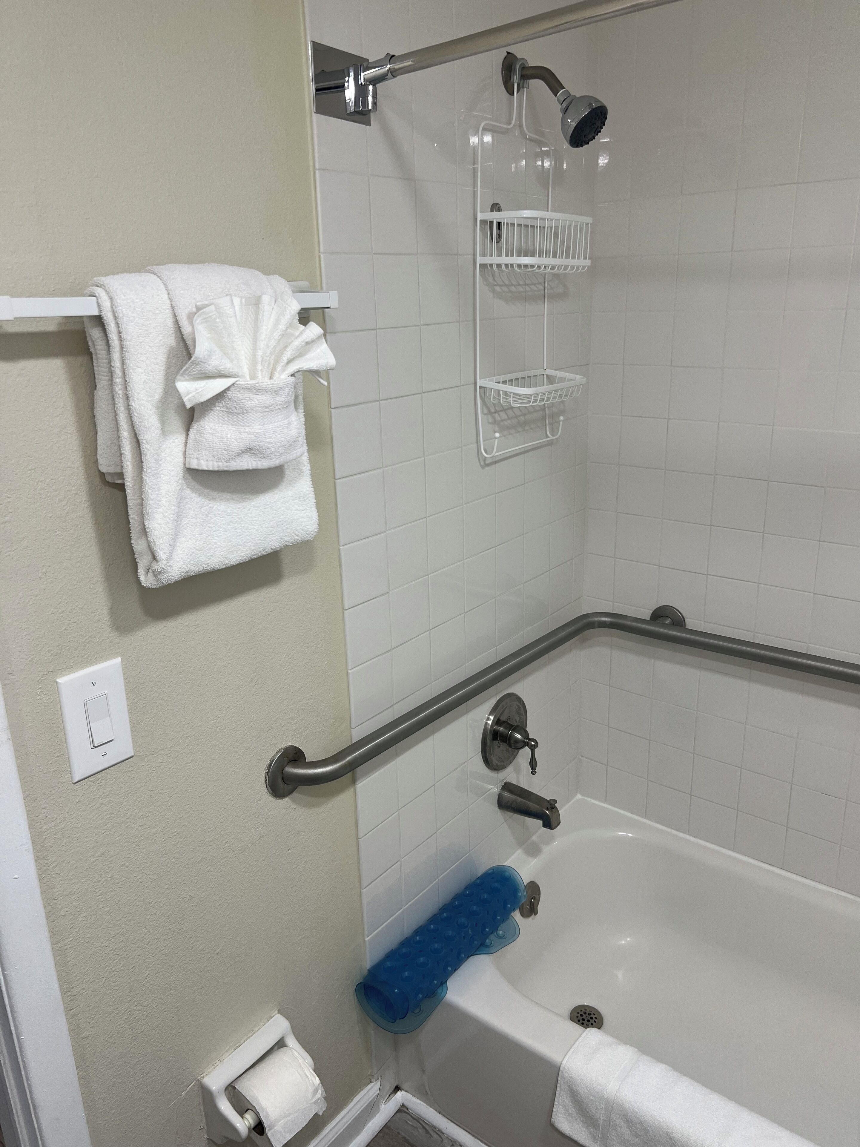 Ein Badezimmer mit einer Badewanne, einer Dusche, einem Handtuchhalter, einem Toilettenpapierhalter und einer Handstange.