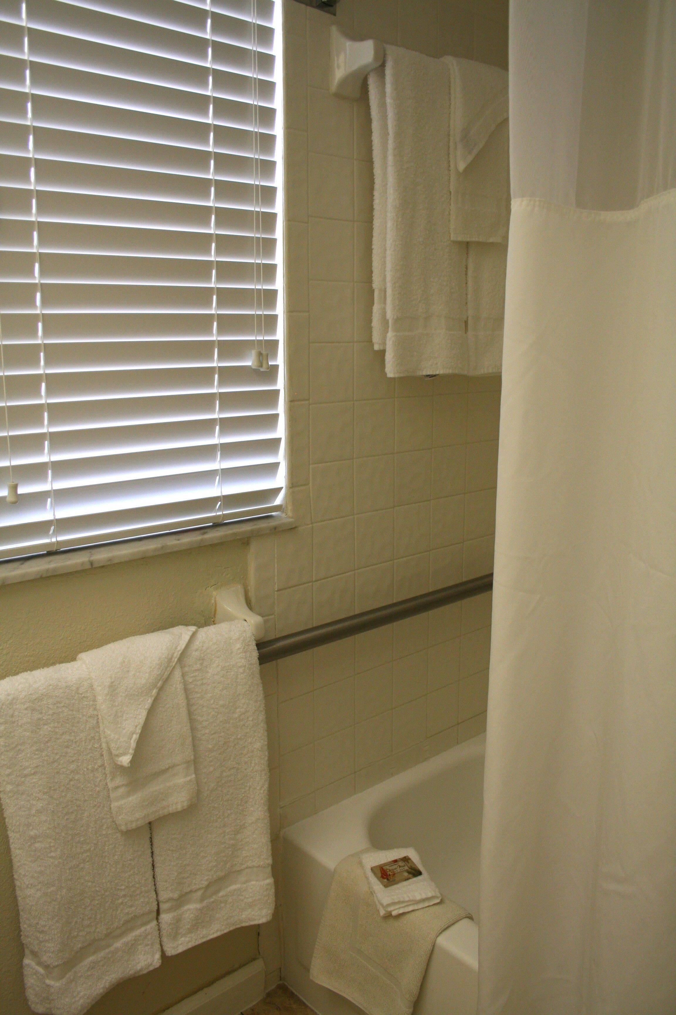 A bathroom with a bathtub, a window with blinds, and a shower curtain.