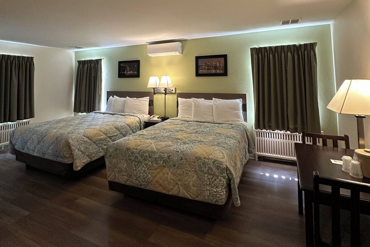 A hotel room with two beds, a desk, a chair, and a radiator.