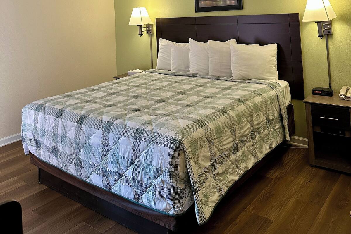 A hotel room with a bed, two bedside lamps, a clock, and a framed picture on the wall.