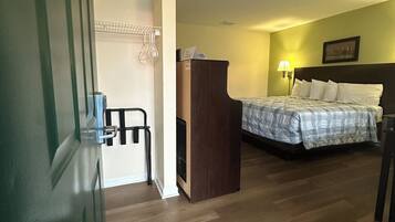Een hotelkamer met een houten vloer, een bed met een geruit sprei, een bureau met stoel, een wandplank en een wandlamp.
