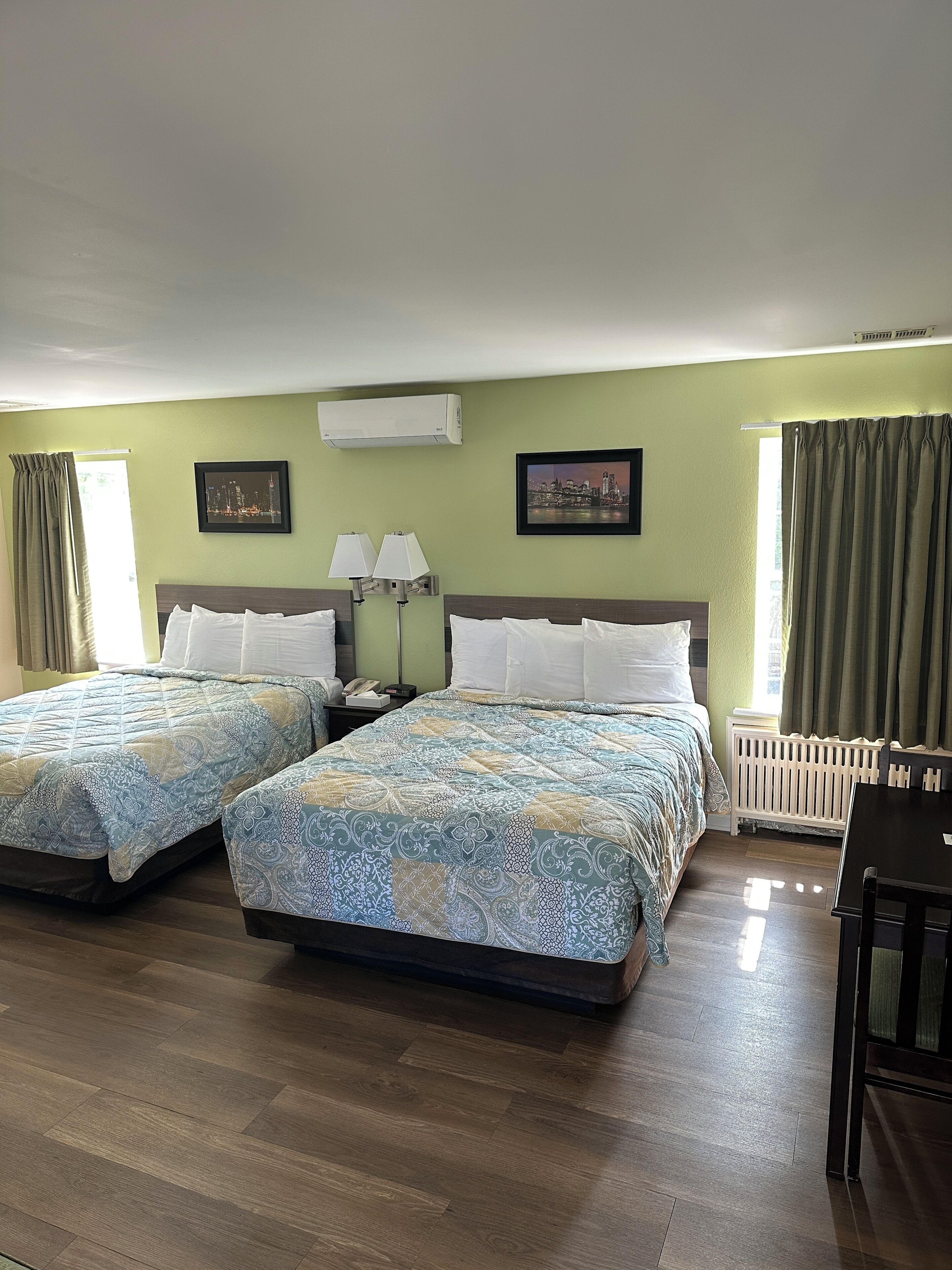 Habitación de hotel con dos camas, un escritorio y una silla. Hay dos lámparas, una ventana con cortinas y un radiador.