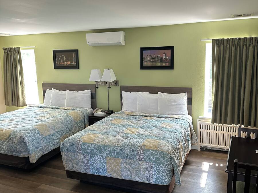 Habitación de hotel con dos camas, un escritorio y una silla. Hay dos lámparas, una ventana con cortinas y un radiador.