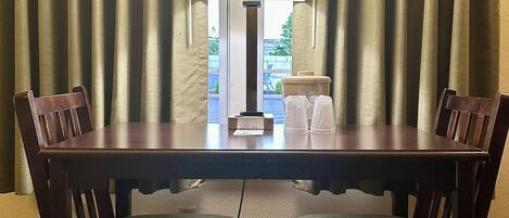 Una mesa de comedor con dos sillas, una lámpara y un ventanal con cortinas.