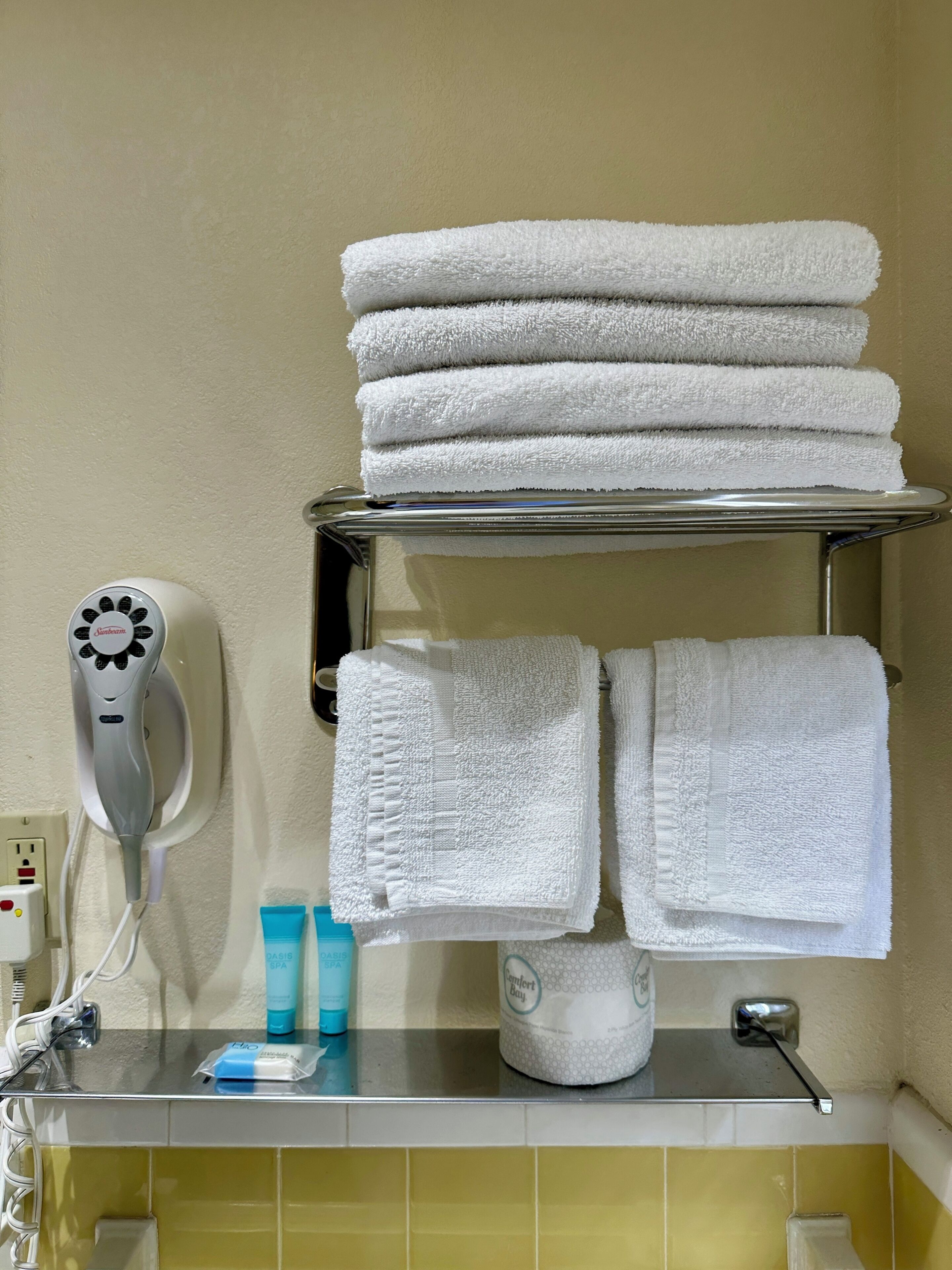 Une salle de bain avec un porte-serviettes sur lequel sont pliées plusieurs serviettes, un sèche-cheveux et des articles de toilette rangés sur une étagère.