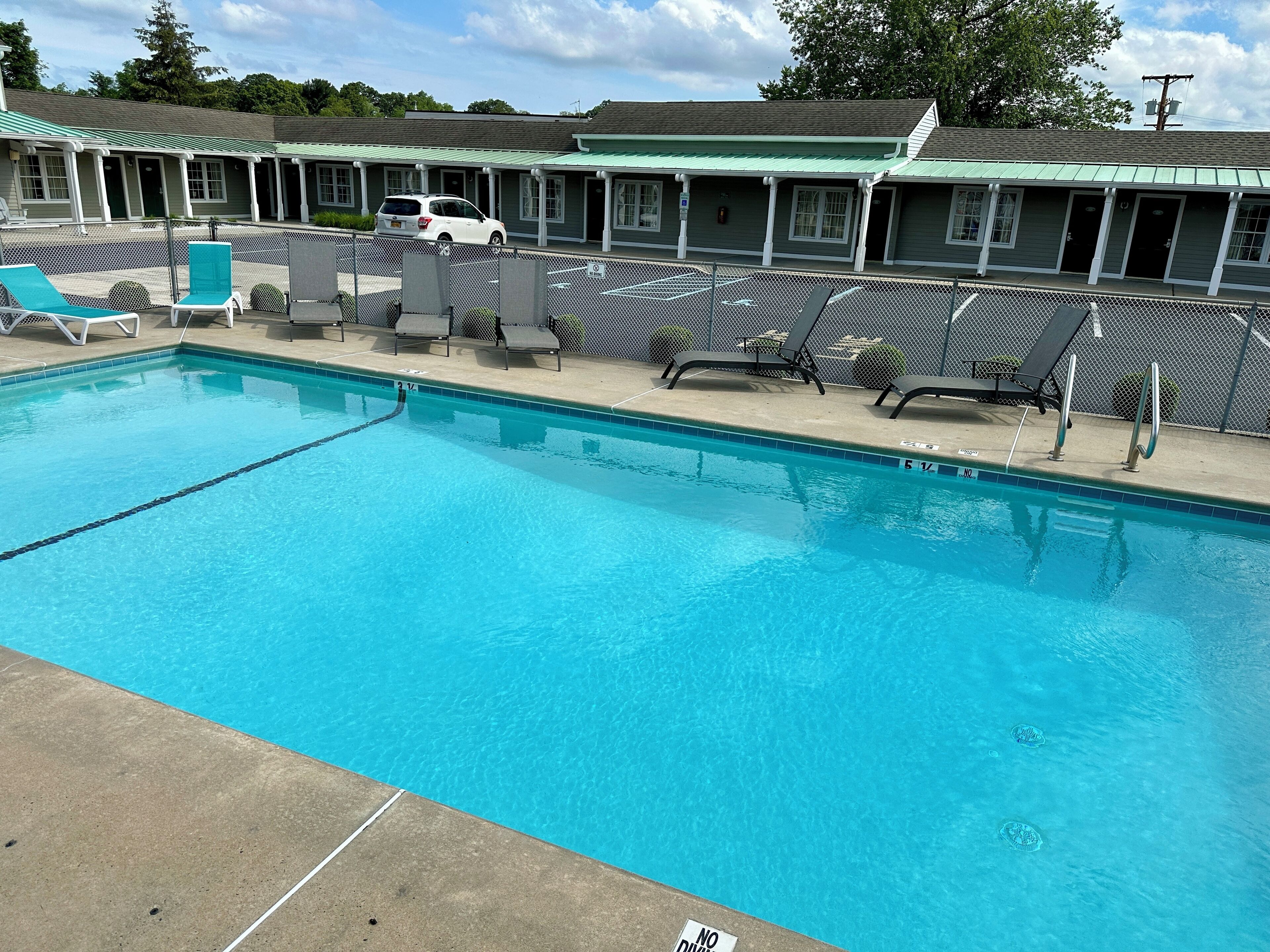 A swimming pool with lounge chairs and a building with multiple rooms in the background.