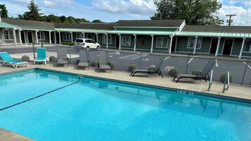 A swimming pool with lounge chairs and a building with multiple rooms in the background.