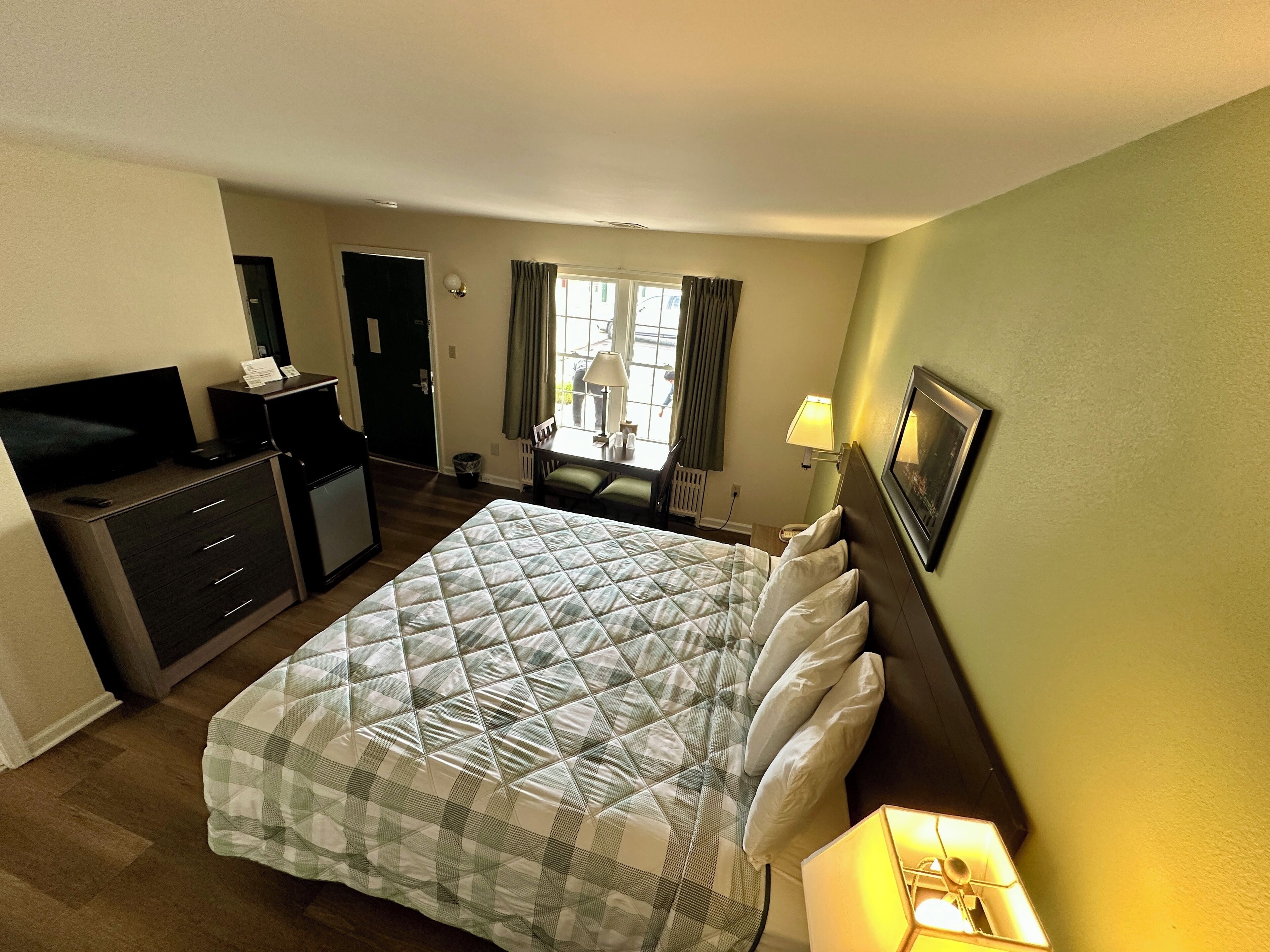 A hotel room with a bed, a desk, a television, and a window with curtains.