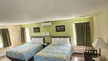 Camera d'albergo con due letti, una scrivania e una sedia. Si vede una finestra con tende, un termosifone e un quadro appeso al muro.