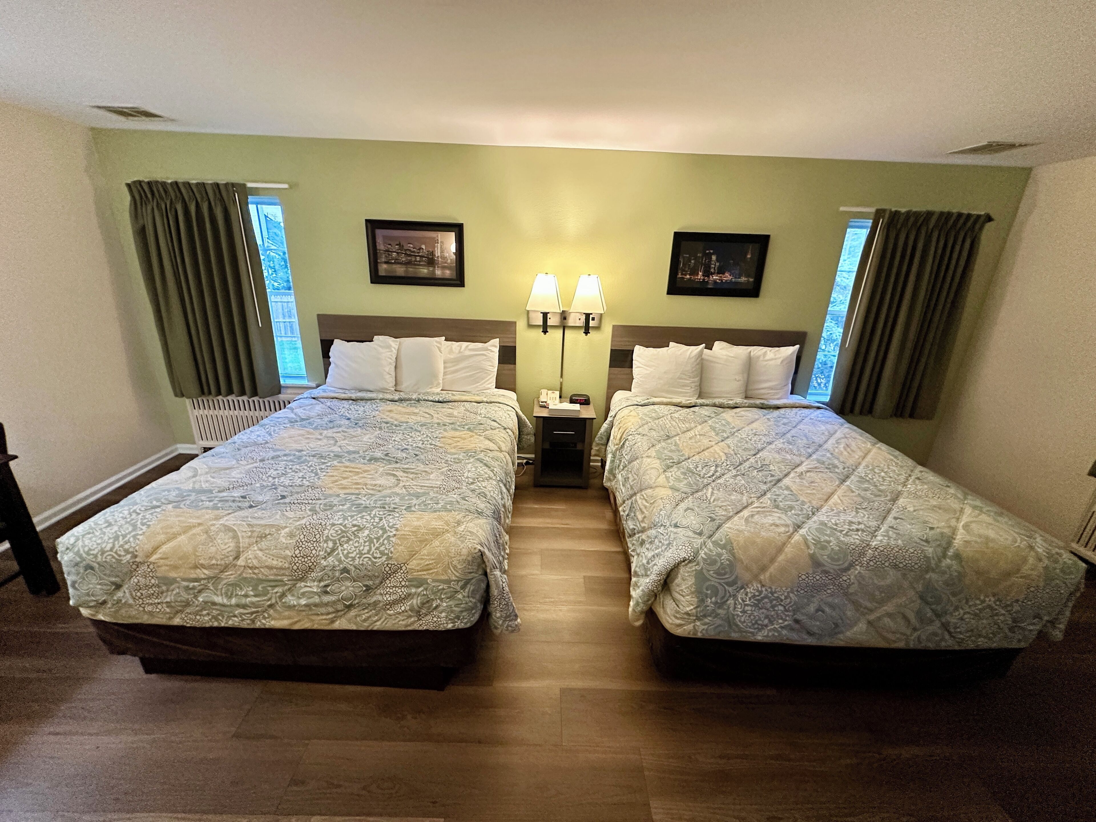 Una habitación de hotel con dos camas, una mesita de noche con lámparas y una ventana con cortinas.