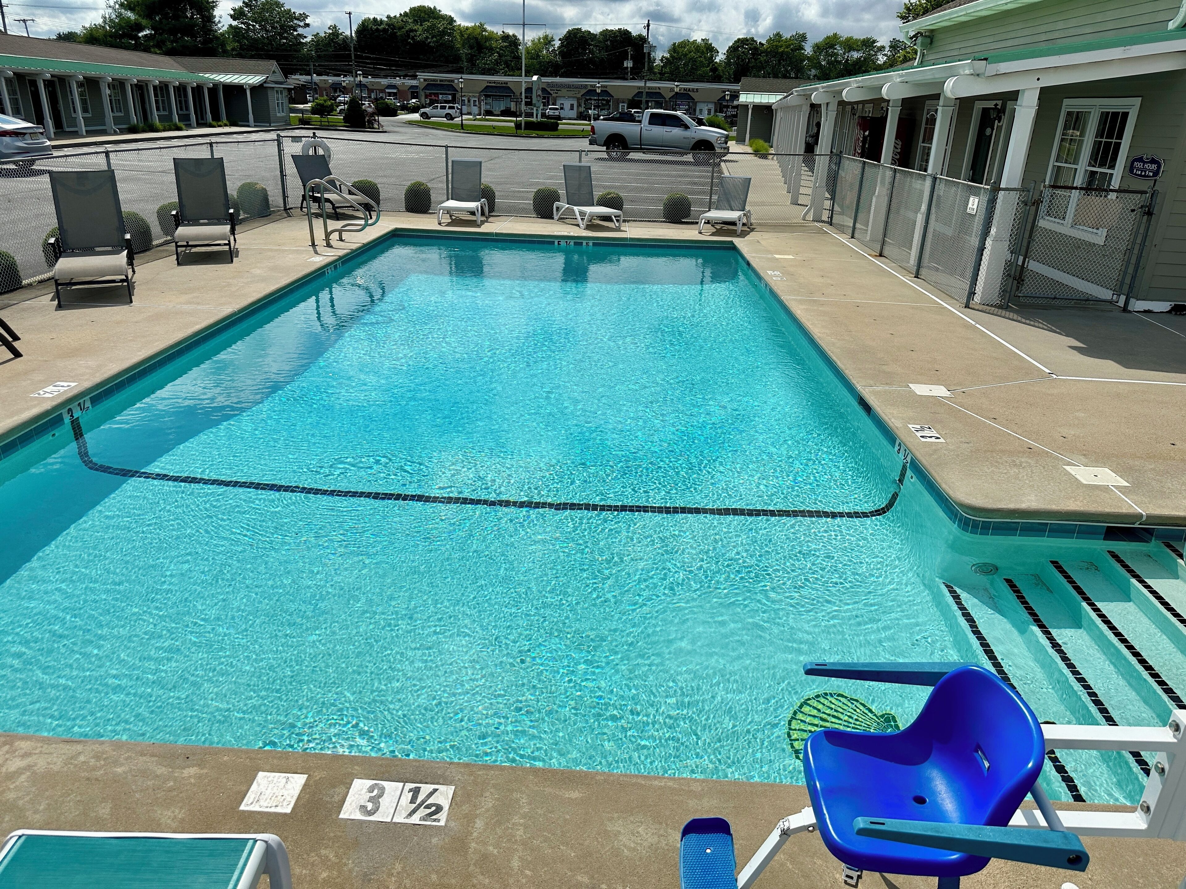 Una piscina rectangular con agua cristalina, rodeada de sillones de descanso y una valla.