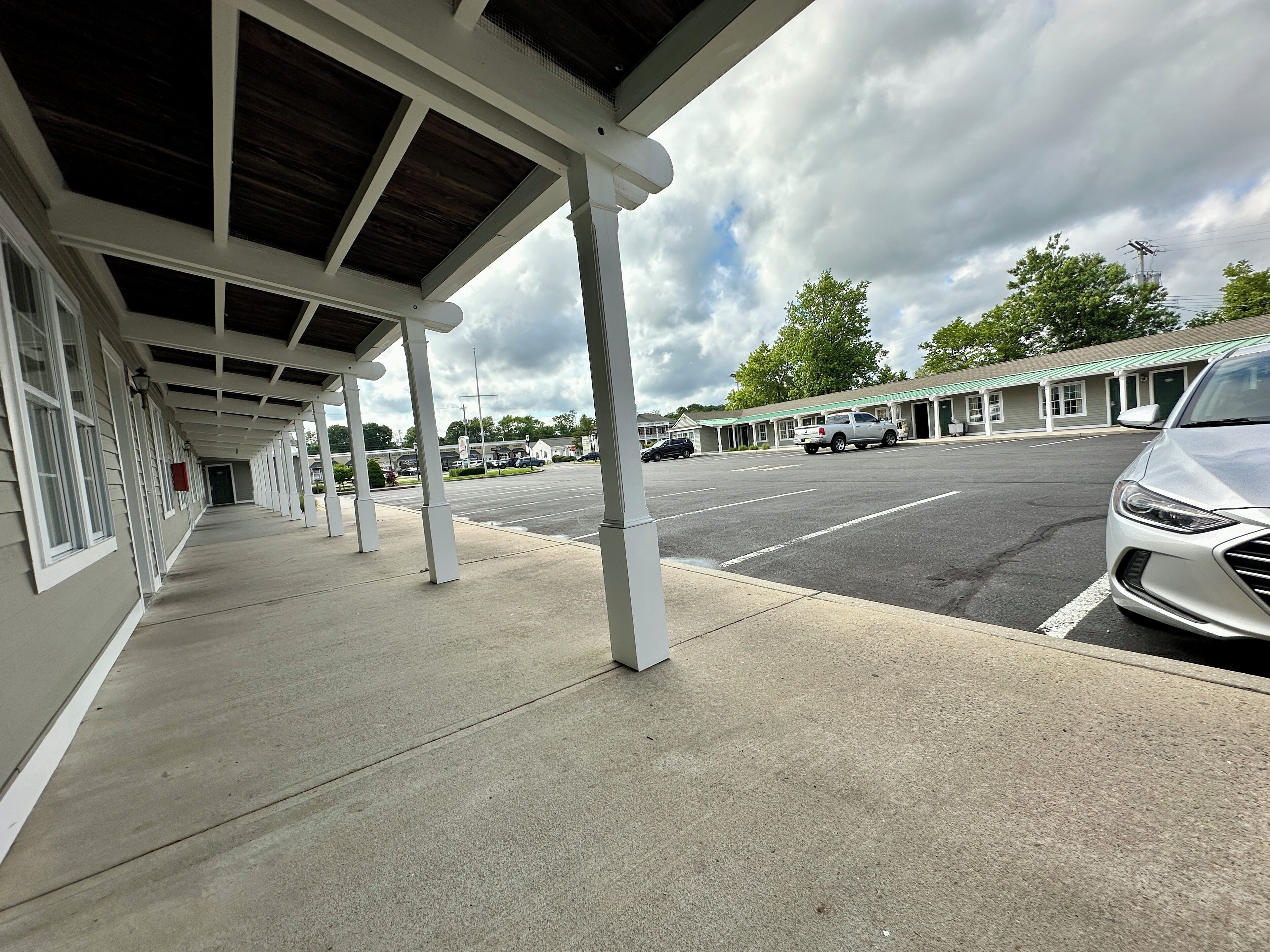A covered outdoor area with a row of motel rooms, a parking lot, and a car parked nearby.