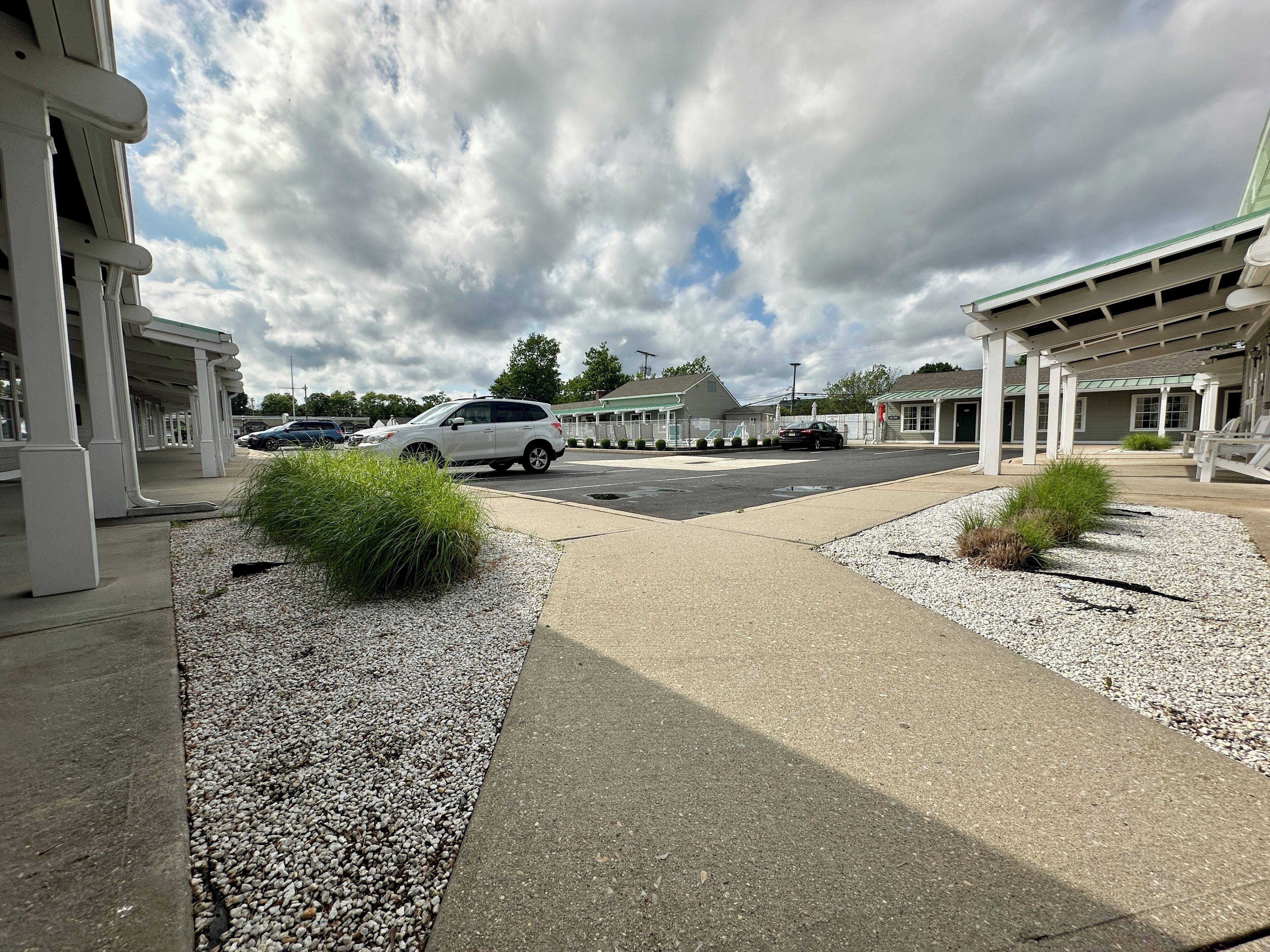A parking area with a white car, gravel landscaping, and a building with a covered walkway.