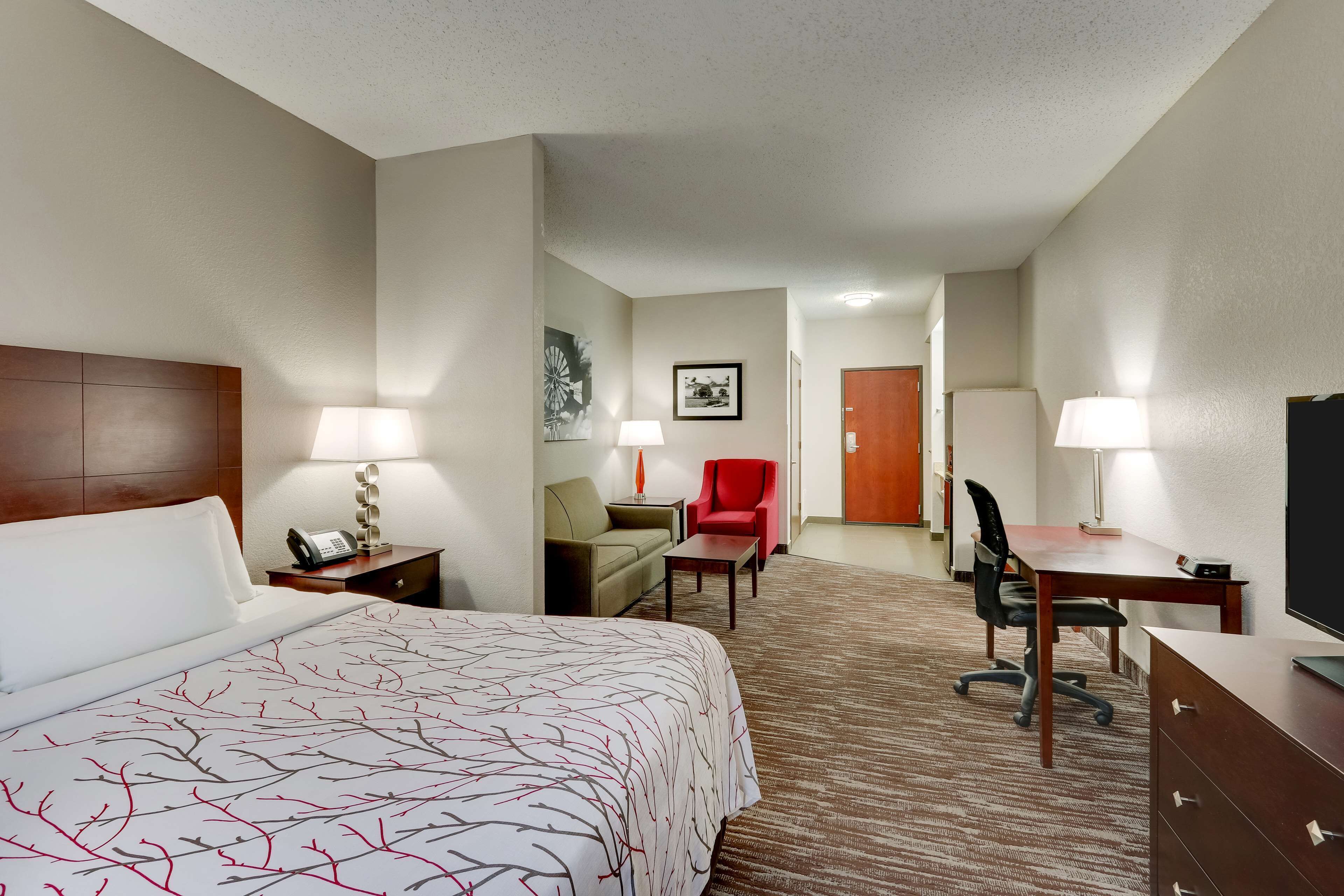 A hotel room with a large bed, a desk, a chair, a TV, and a red armchair.