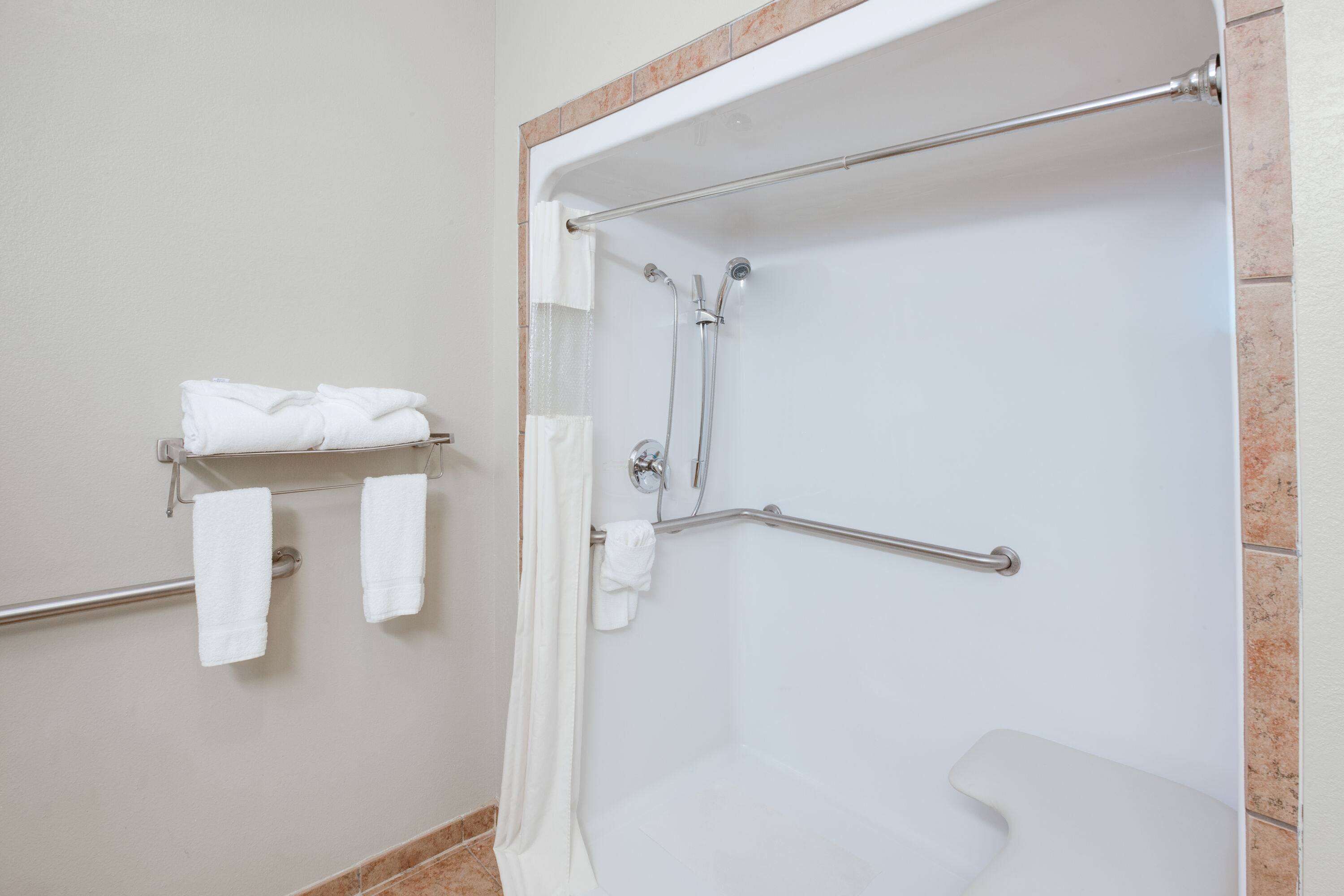 Bagno con doccia, maniglie di sostegno e porta asciugamani con asciugamani piegati.