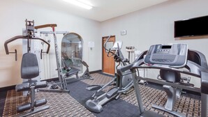 Un gimnasio con diversos equipos de ejercicio, una cinta de correr y un televisor montado en la pared.