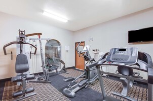 Un gimnasio con diversos equipos de ejercicio, una cinta de correr y un televisor montado en la pared.