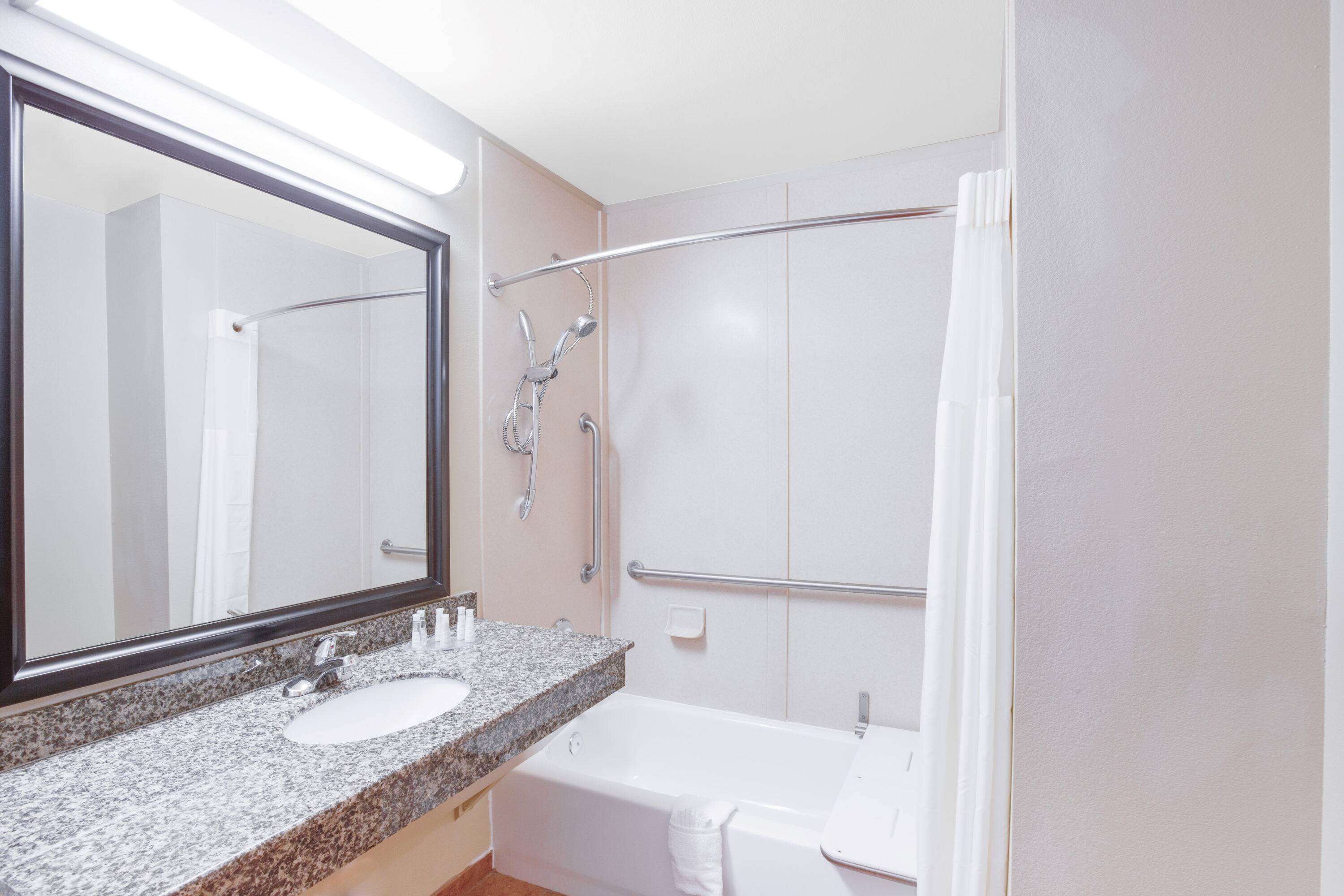 A bathroom with a granite countertop sink, a large mirror, a bathtub, and a shower with a glass door.