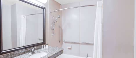 A bathroom with a granite countertop sink, a large mirror, a bathtub, and a shower with a glass door.