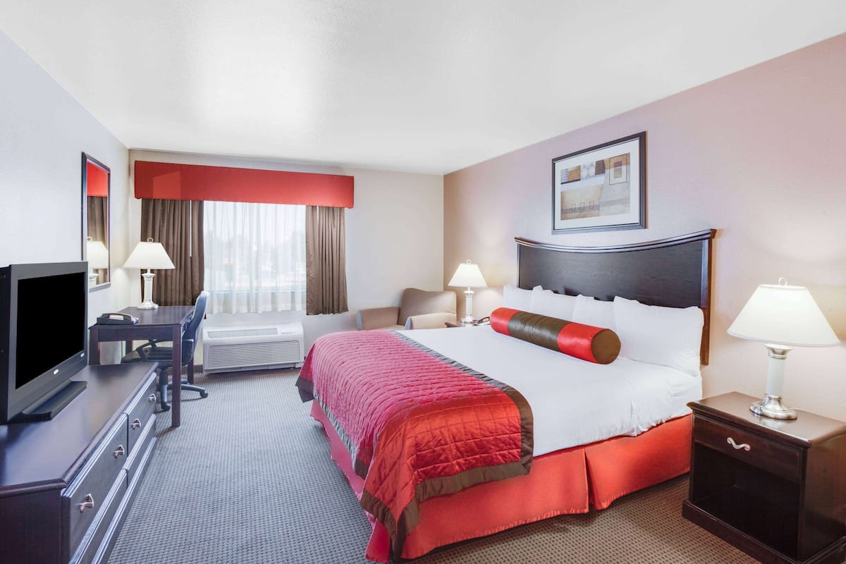 Een hotelkamer met een bed, een bureau, een televisie en een raam met gordijnen.