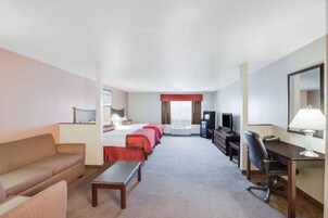 Una habitación de hotel con cama, sofá, escritorio, silla, televisor y lámpara de escritorio.