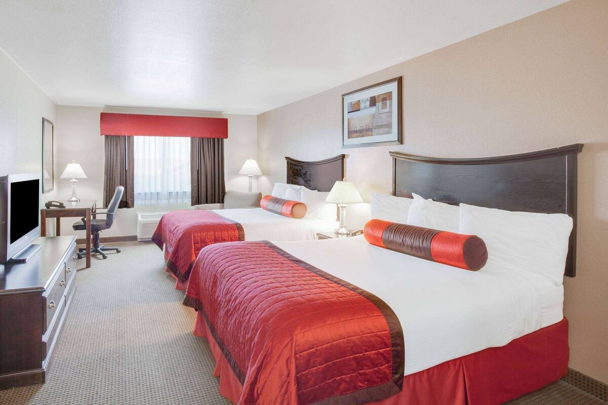 Een hotelkamer met twee bedden, een bureau met een stoel, een televisie en een raam met gordijnen.