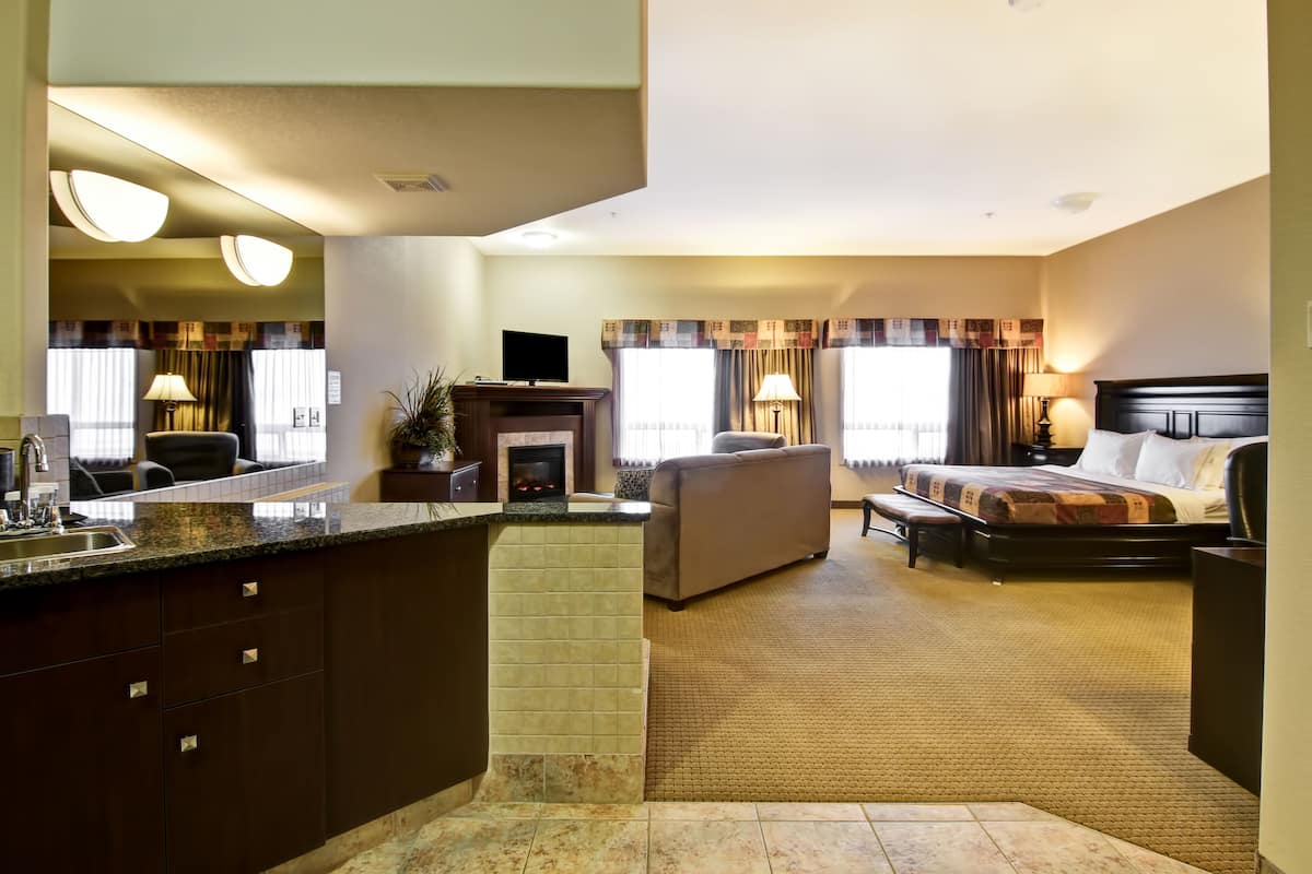 A hotel room with a kitchenette, a sofa, a bed, and a fireplace.