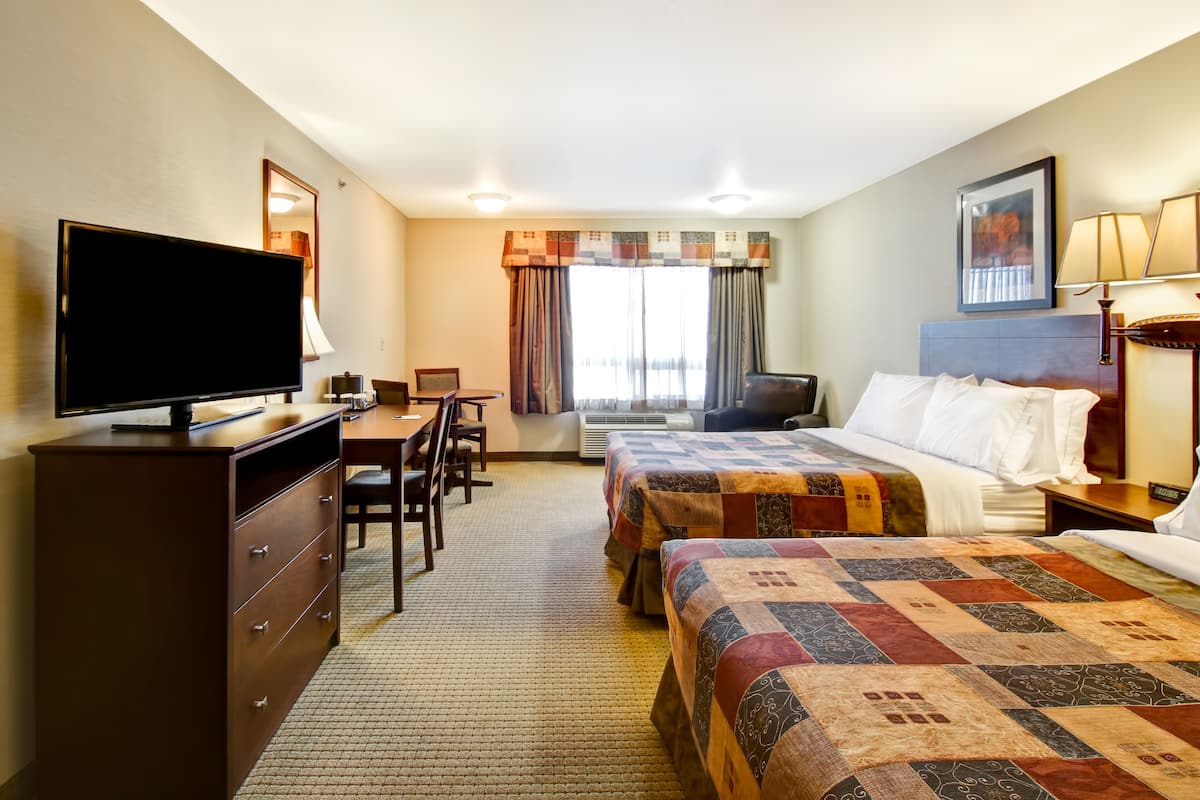 A hotel room with two beds, a desk, a television, and a window with curtains.