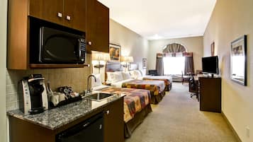 Quarto de hotel com cozinha compacta, duas camas, televisão e uma janela grande.