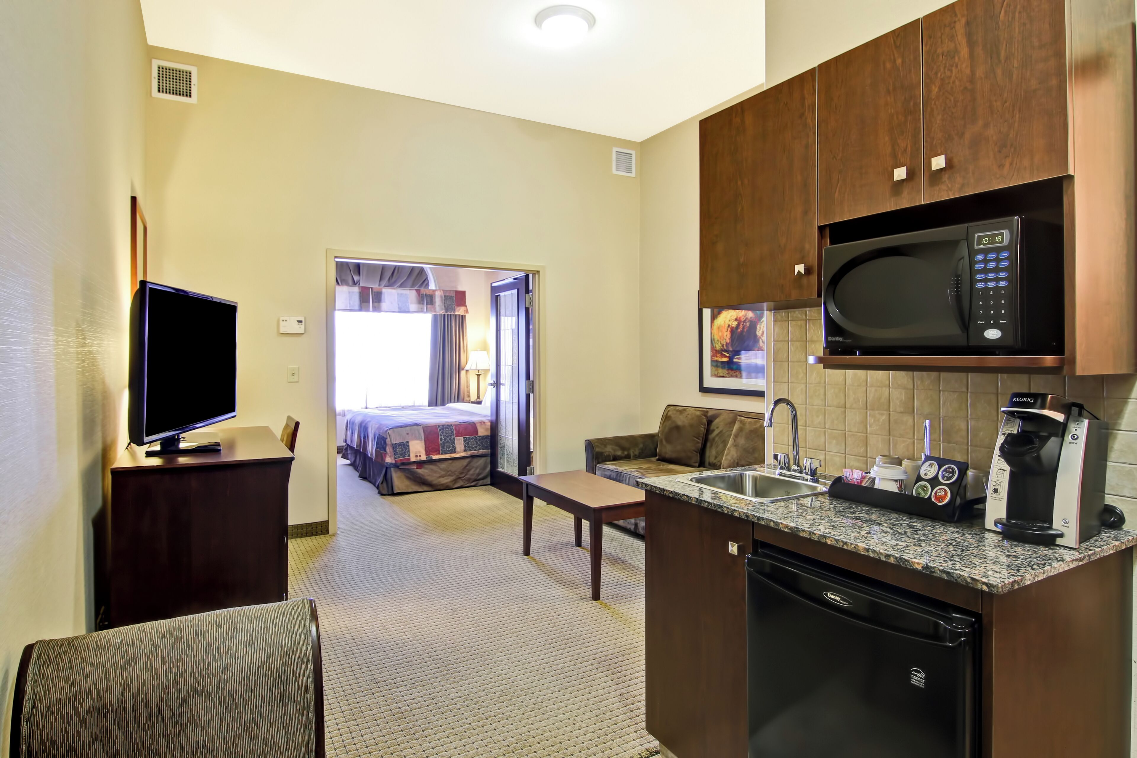 A compact hotel room with a kitchenette, a flat-screen TV, a sofa, and a bed with a view.