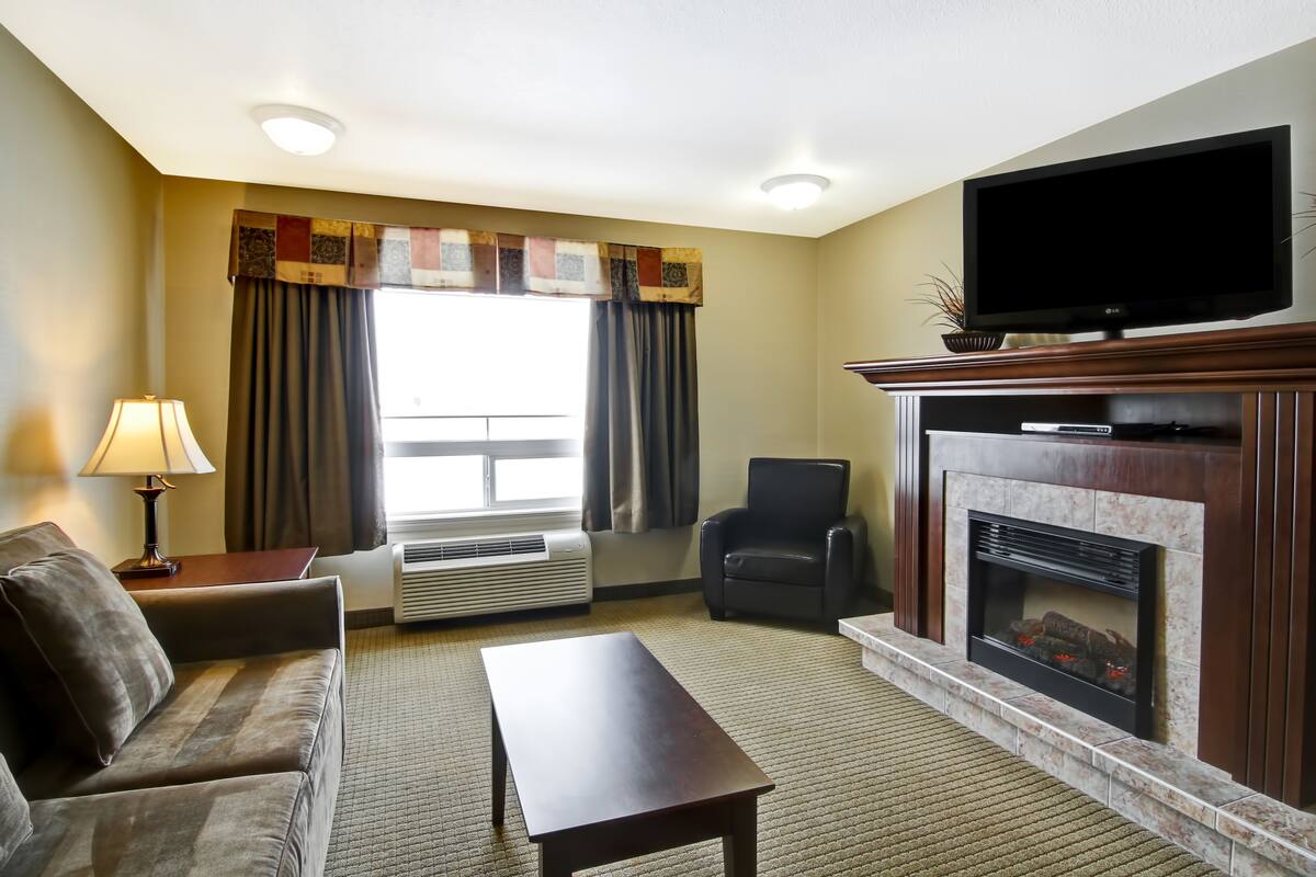 A hotel room with a sofa, a coffee table, a TV, a fireplace, and a window with curtains.