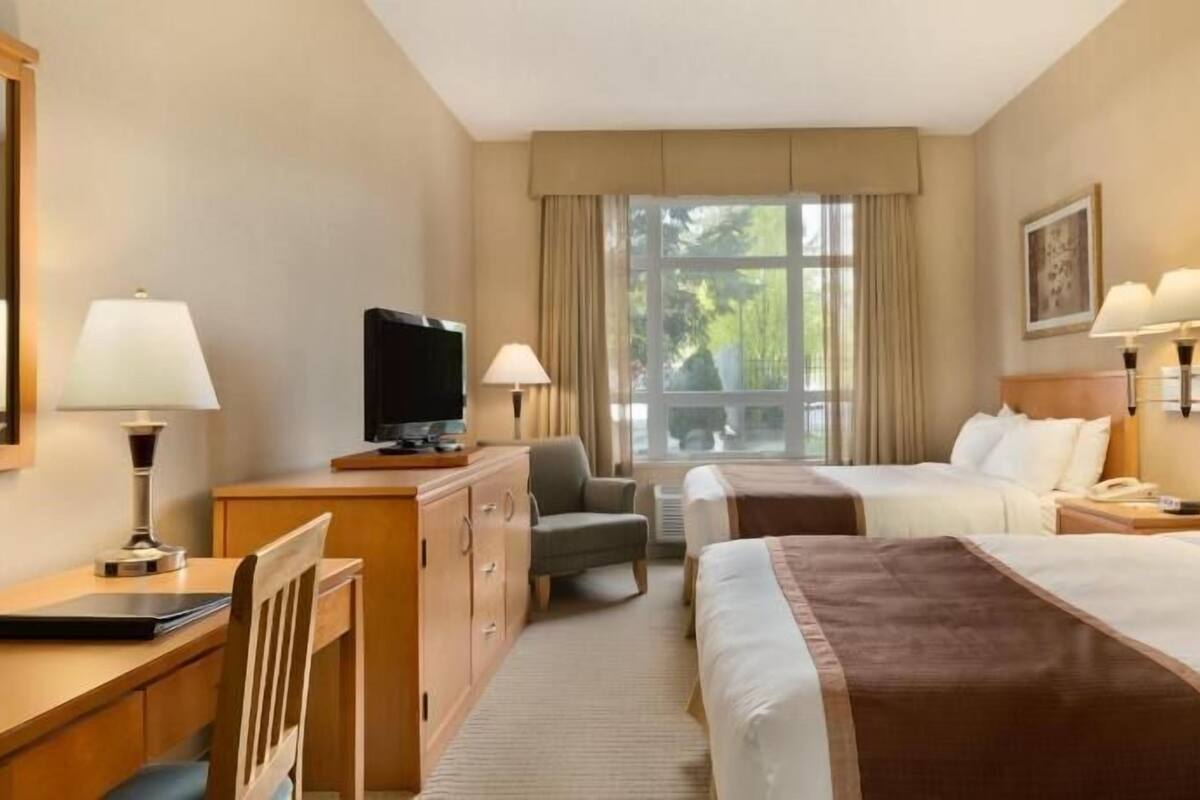 Habitación de hotel con dos camas, un escritorio, una televisión y una ventana con vistas a zonas verdes.
