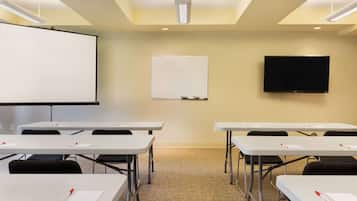 Una sala conferenze con tavoli bianchi, sedie nere, una lavagna e un televisore a schermo piatto.
