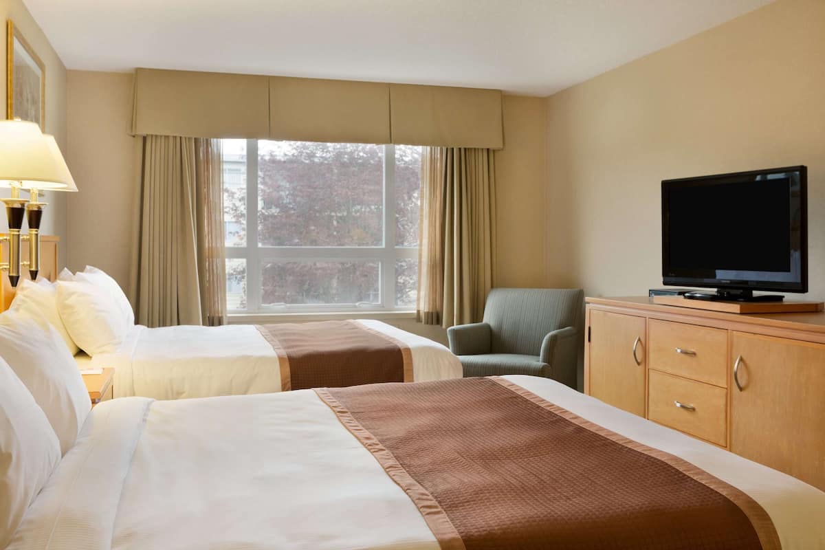 Una habitación de hotel con dos camas, un televisor sobre un mueble de madera y una ventana con cortinas.