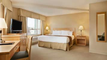 A hotel room with a bed, desk, chair, television, lamps, and a mirror.