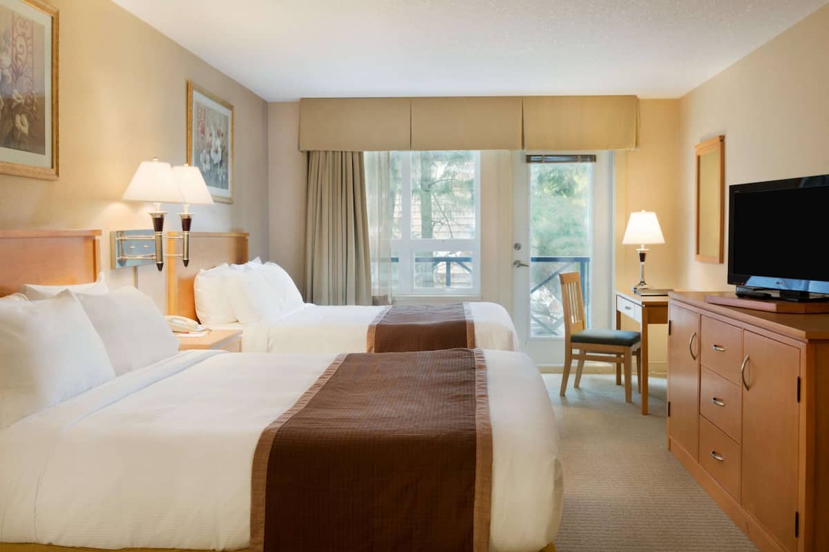 Habitación de hotel con dos camas, un escritorio, un televisor y vistas al exterior.