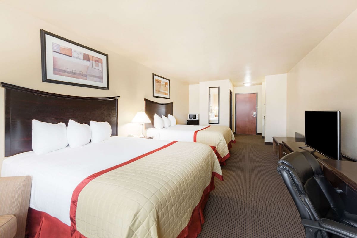A hotel room with two beds, a TV, a desk, and a chair.