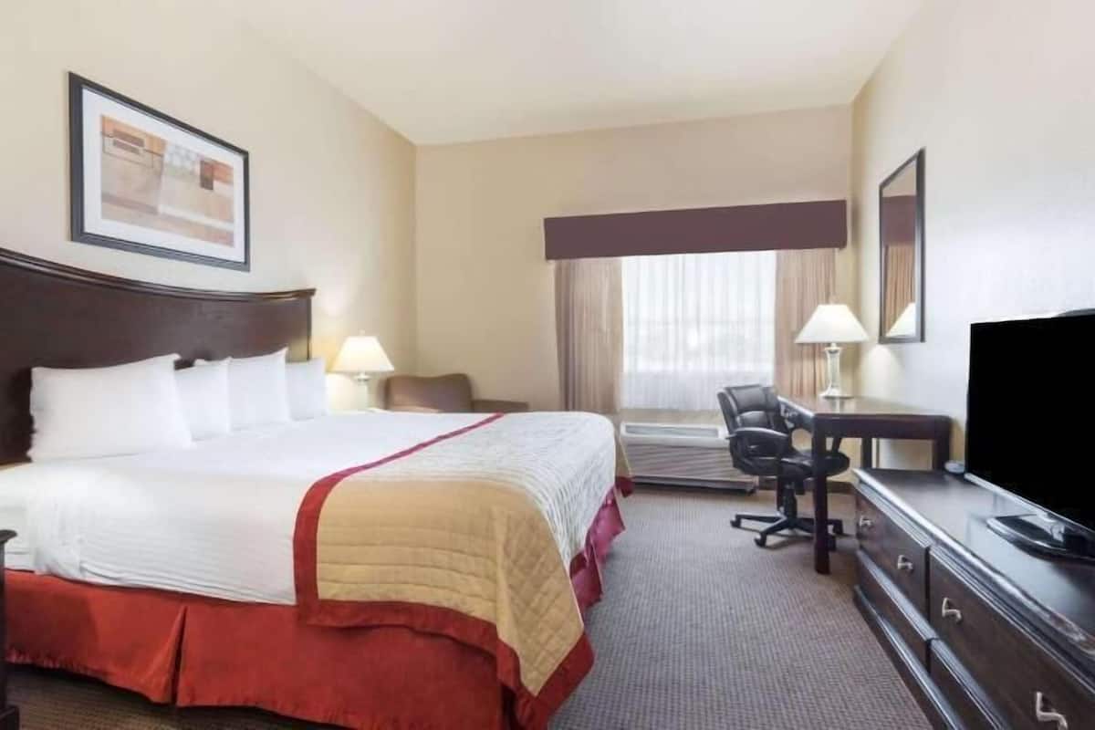 A hotel room with a bed, a desk with a TV, a chair, and a window with curtains.