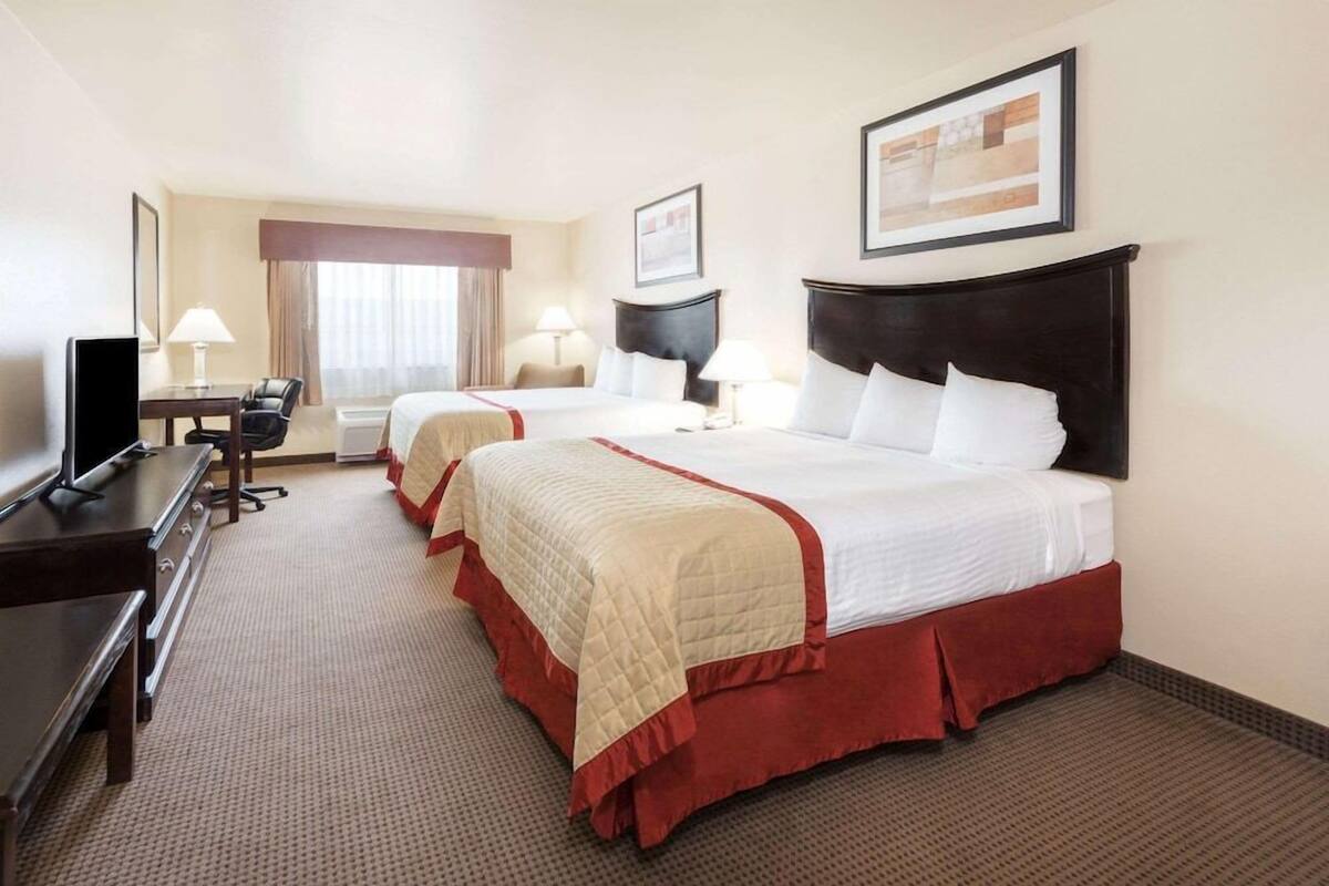 A hotel room with two beds, a desk, a TV, and a window with curtains.