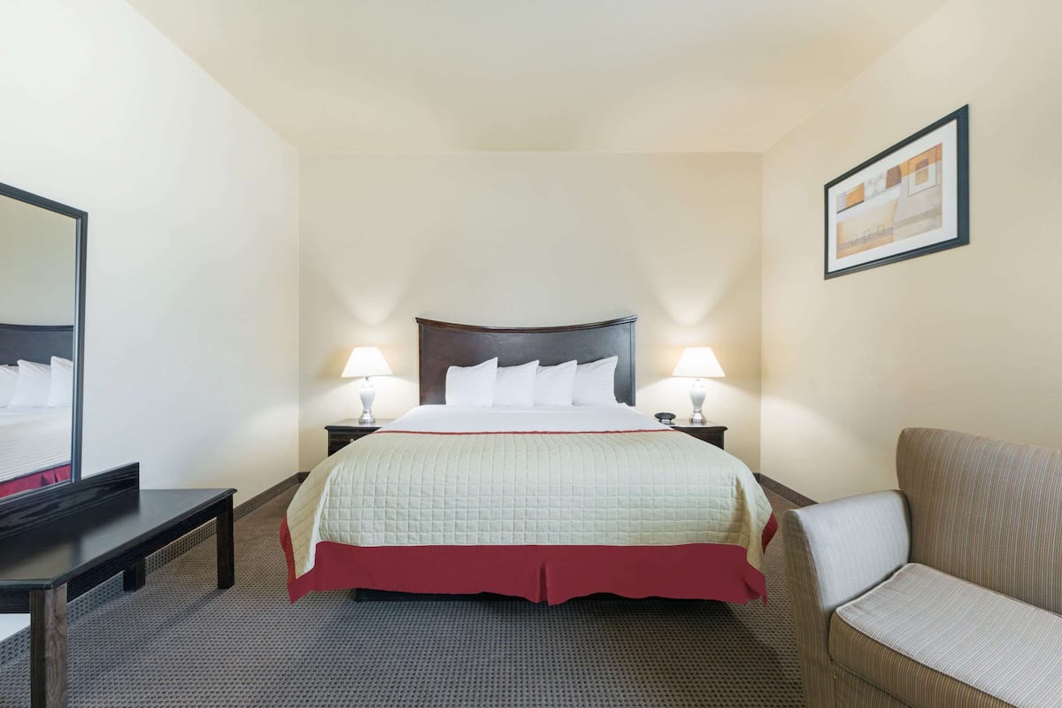 A hotel room with a bed, bedside lamps, a chair, a desk, and a mirror.