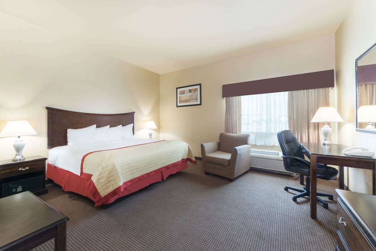 A hotel room with a bed, desk, chair, and a window with curtains.