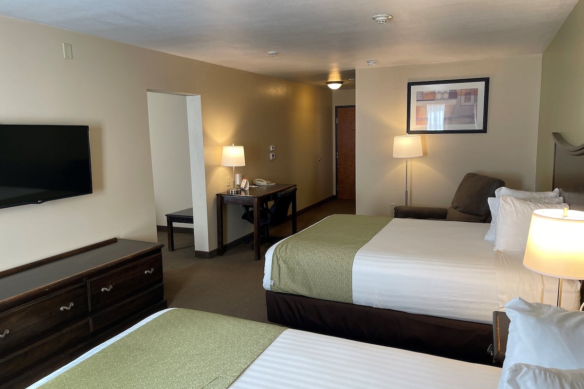 A hotel room with two beds, a desk, a chair, a television, and a lamp.