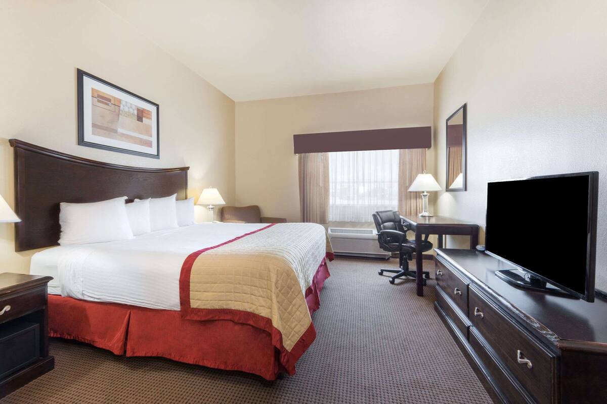 A hotel room with a large bed, a desk with a TV, a chair, and a desk lamp.